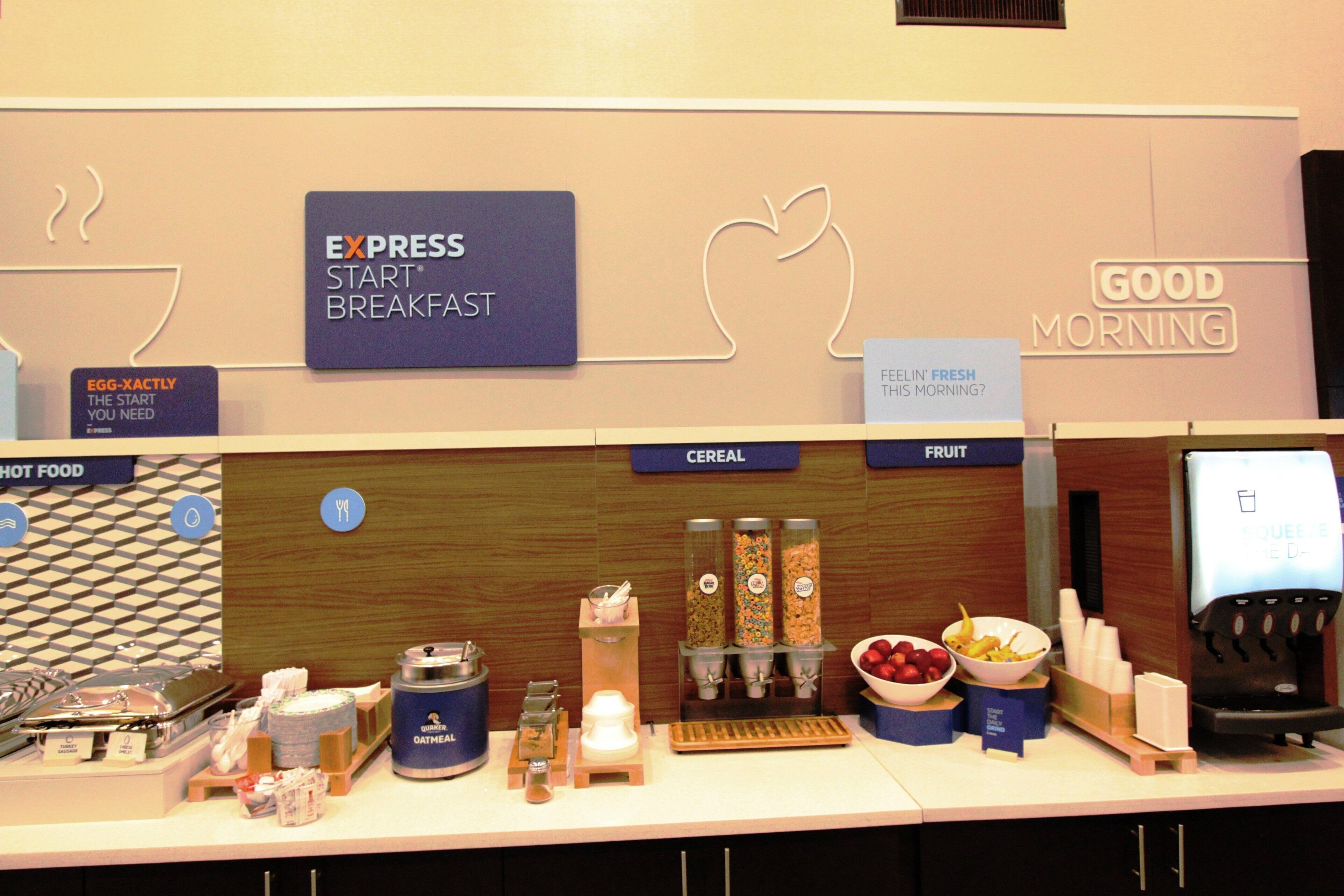 Zona de desayuno tipo buffet con secciones identificadas para cereales, fruta y comida caliente.