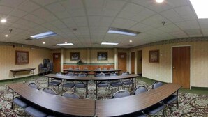 Une salle de conférence dotée d’une grande table ovale, de nombreuses chaises, d’une petite scène et d’un sol recouvert de moquette.