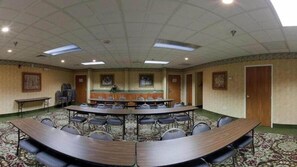 A conference room with a large oval table, multiple chairs, a small stage, and a carpeted floor.