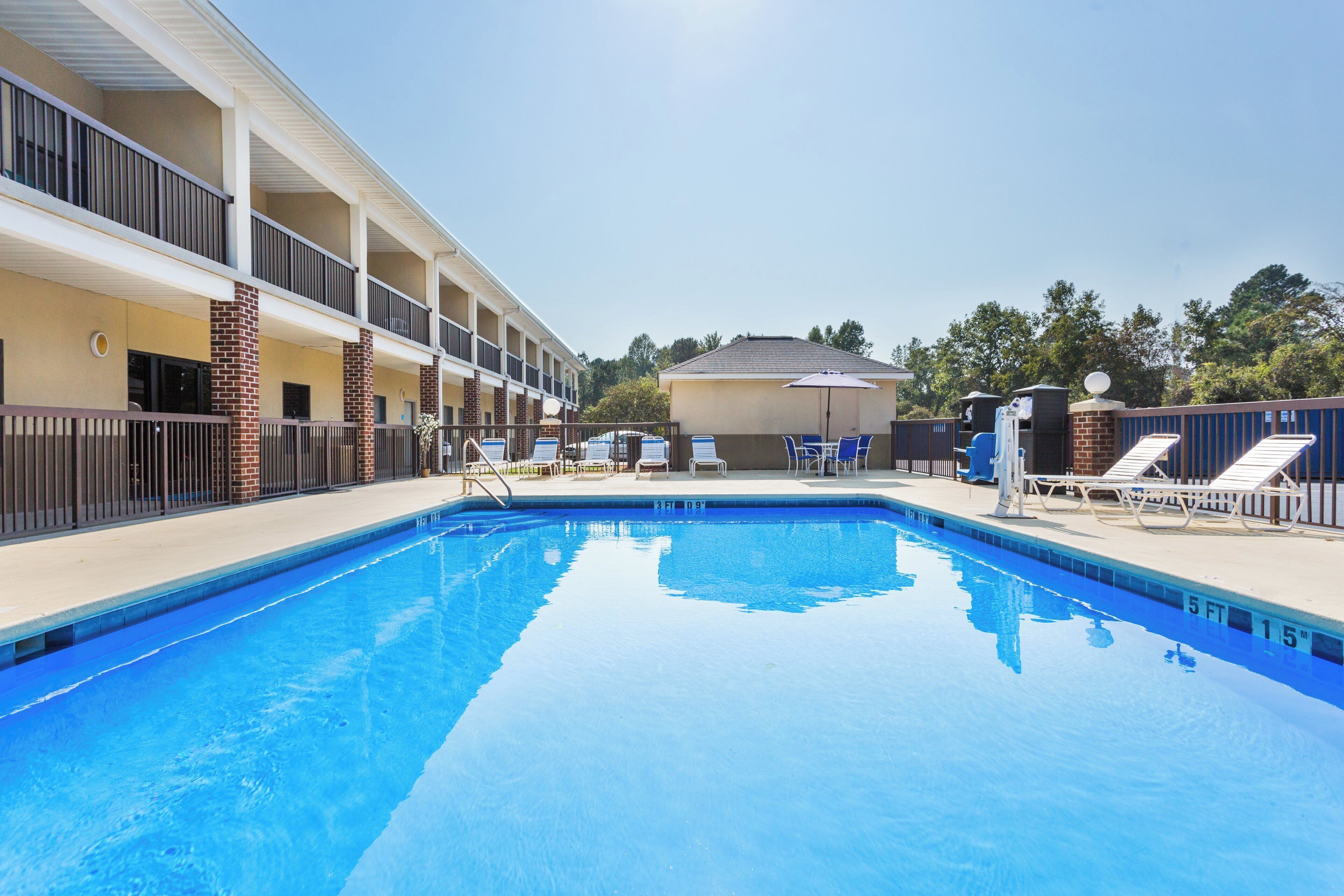 A swimming pool with lounge chairs and a building with multiple floors and balconies.