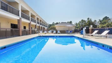 A swimming pool with lounge chairs and a building with multiple floors and balconies.