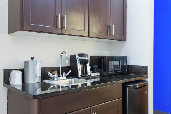A kitchenette with a coffee maker, microwave, sink, and cabinets.