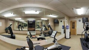 Une salle de sport équipée de matériel d’exercice, de miroirs et d’un téléviseur.