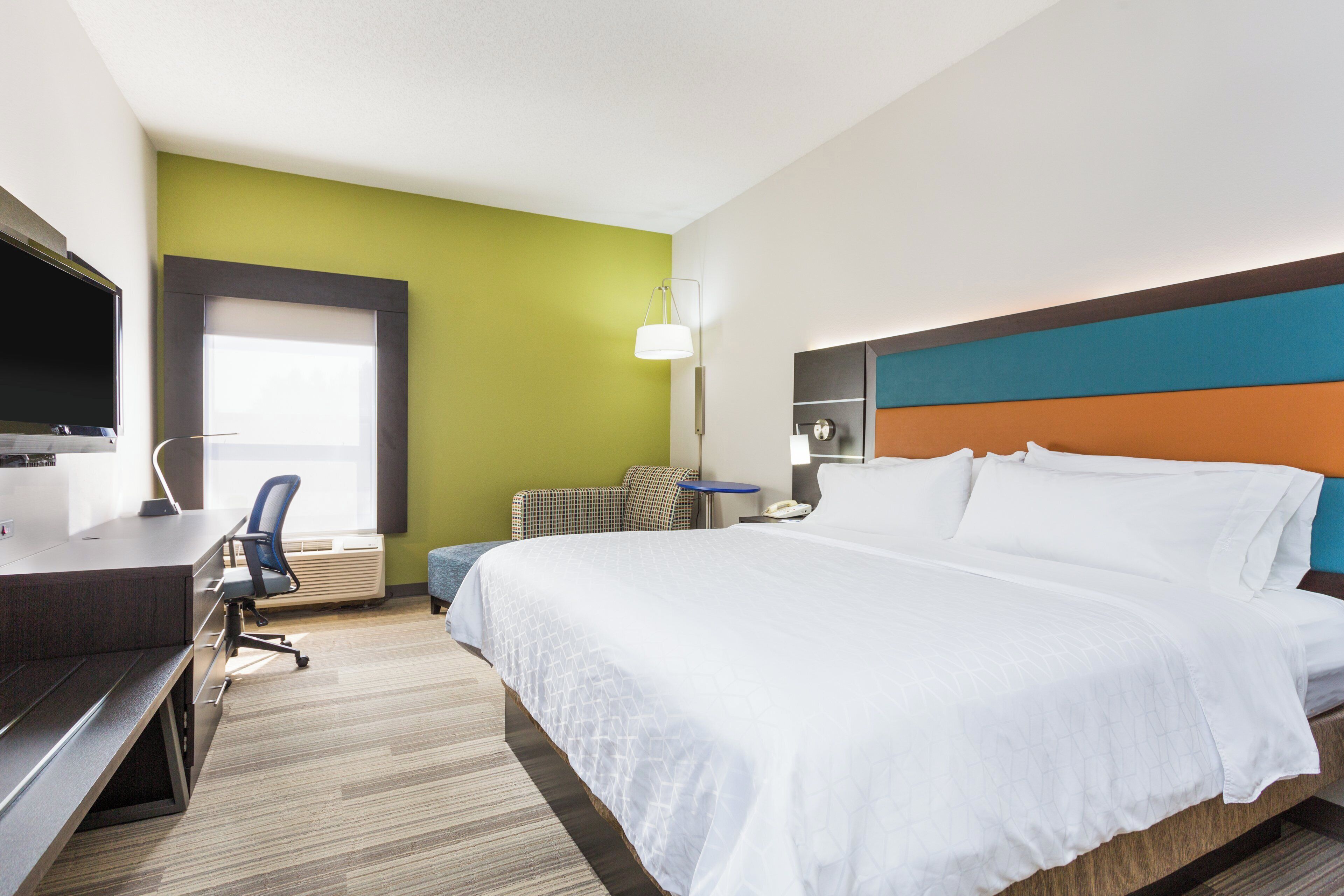 A hotel room with a bed, a desk with a computer, a chair, a lamp, and a television.