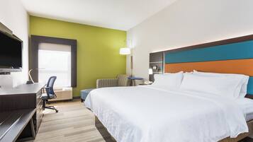 A hotel room with a bed, a desk with a computer, a chair, a lamp, and a television.