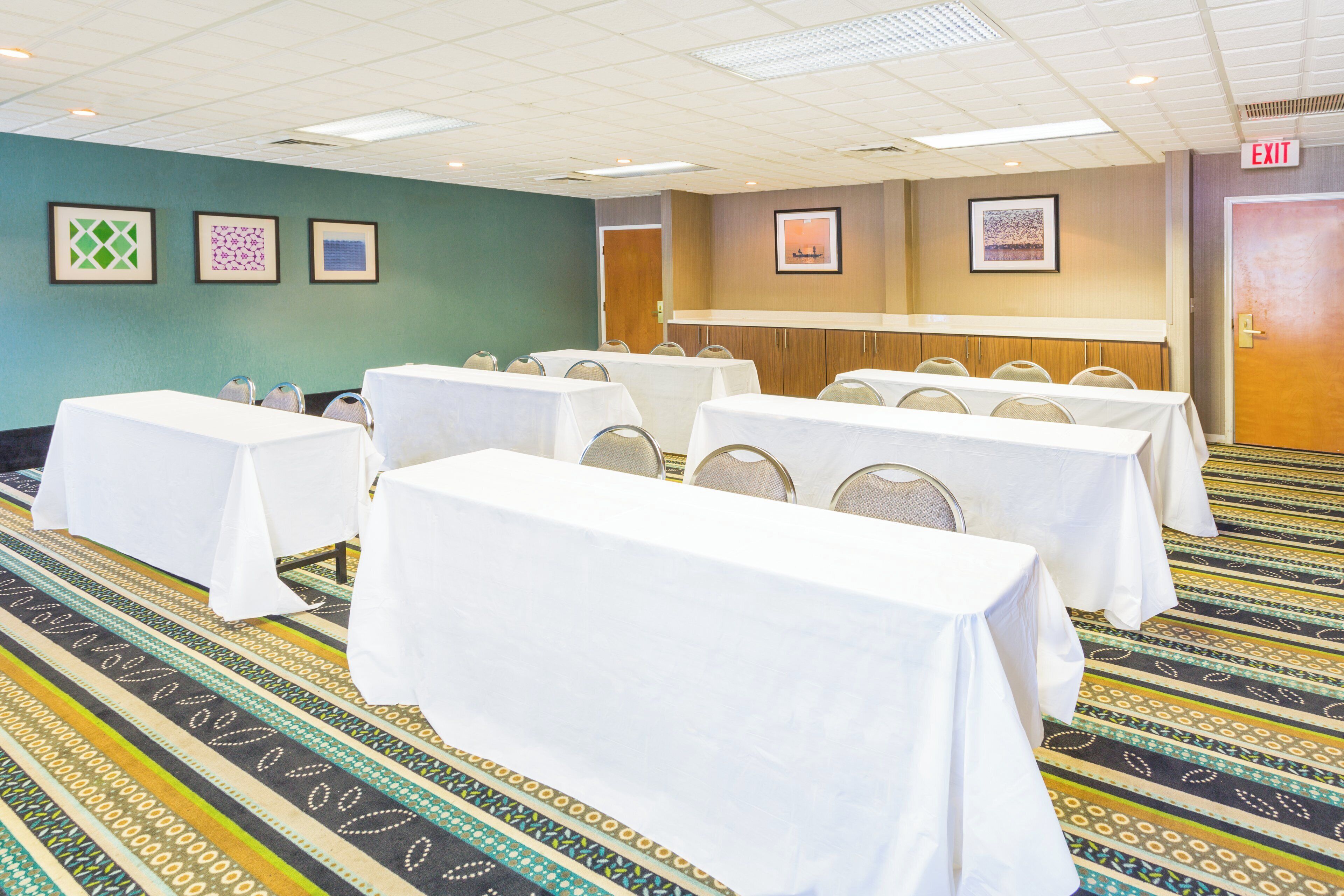 A conference room with tables set up for meetings, a patterned carpet, and framed artwork on the walls.