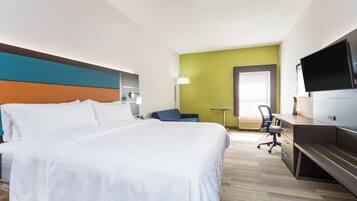 A hotel room with a large bed, a desk, a chair, a television, and a door leading to another room.