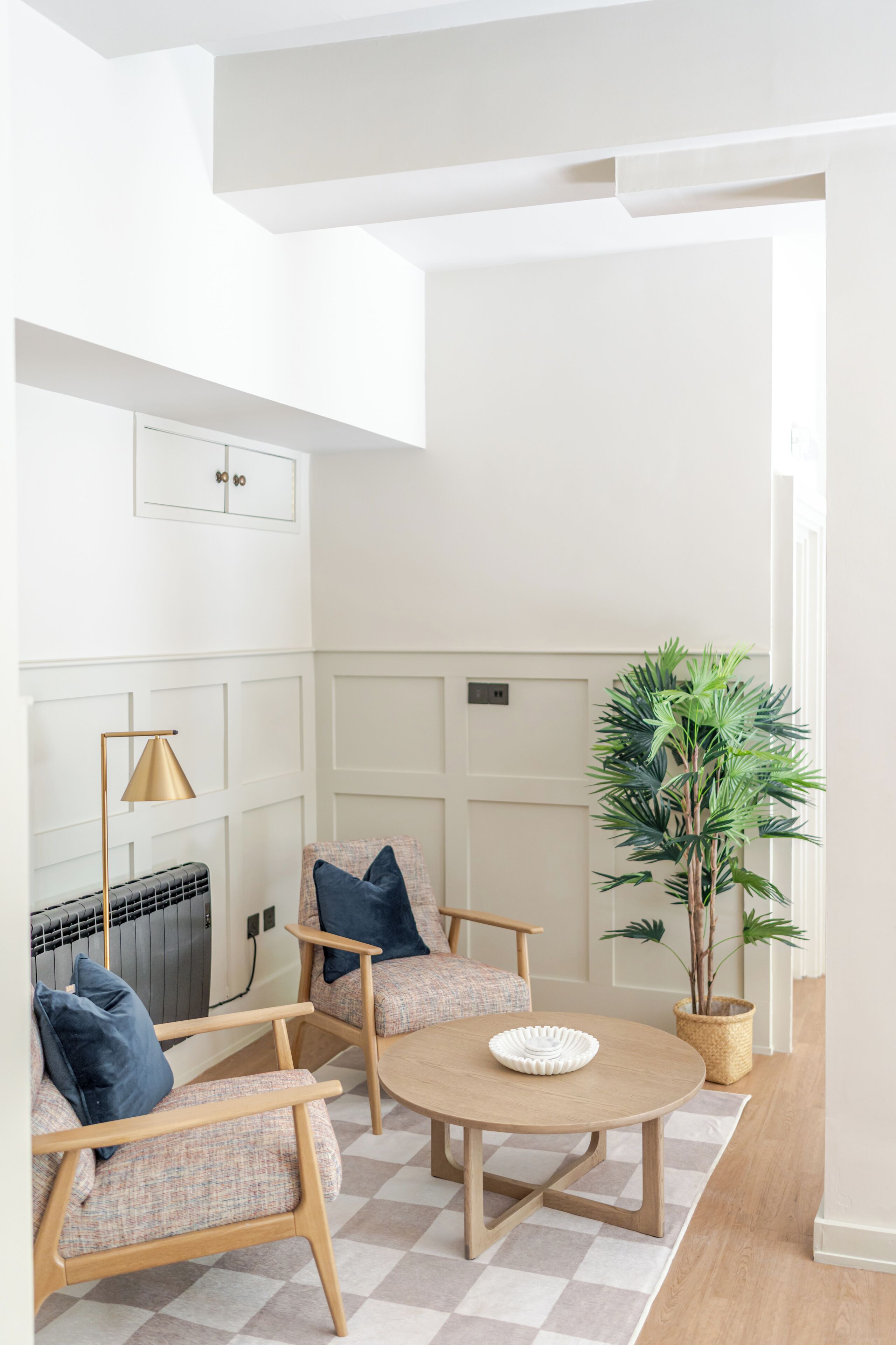 Una sala de estar moderna con una mesa redonda de madera, dos sillones, una lámpara de pie y una planta en maceta.