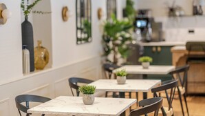 A modern dining area with marble tables, black chairs, and potted plants.
