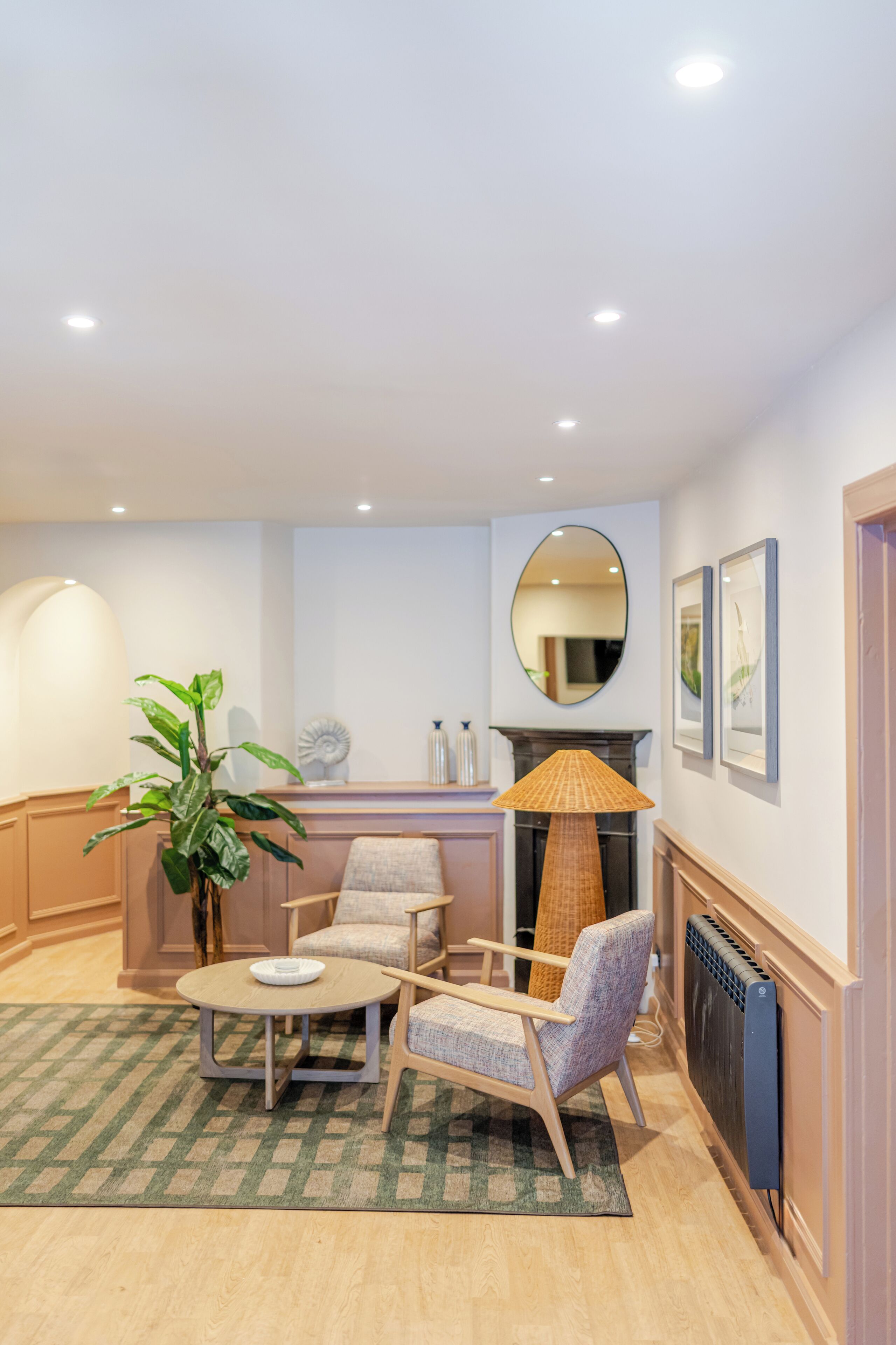 A cozy living room with a round table, two armchairs, a large potted plant, a fireplace, and framed pictures on the wall.