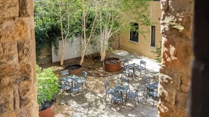 An outdoor patio with stone flooring, metal chairs, and tables, surrounded by trees and a brick wall.