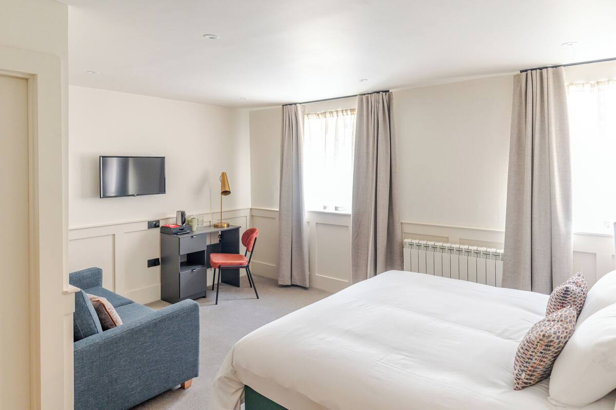 A hotel room with a bed, a desk, a chair, a television, and a window with curtains.