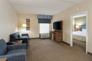 A hotel room with a sofa, a desk with a lamp, a flat-screen TV, a bed, and a window with a view. - Hampton Inn Buffalo South/I-90 (Buffalo)