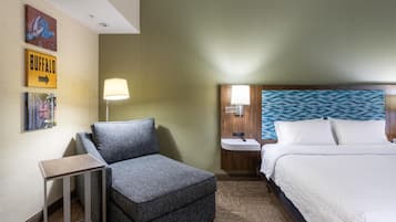 Une chambre d’hôtel avec un lit, une table de chevet, une lampe, une chaise et une petite table.