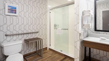 A modern bathroom with a glass shower enclosure, a toilet, a vanity with a mirror, and a towel rack.