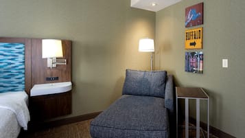 Une chambre d’hôtel comprenant un lit, un petit canapé, une table de chevet, une lampe, une étagère fixée au mur et une œuvre d’art décorative.