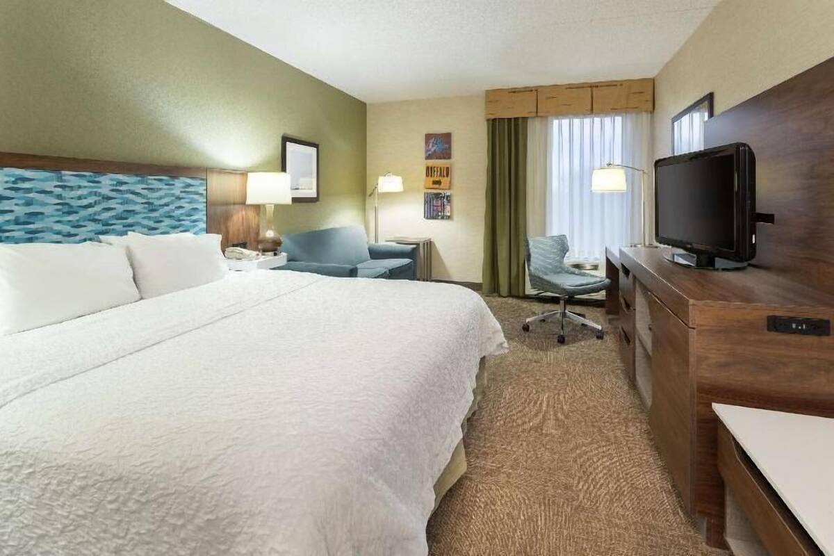 Une chambre d’hôtel avec un grand lit, un bureau avec une télévision, une chaise et une lampe.