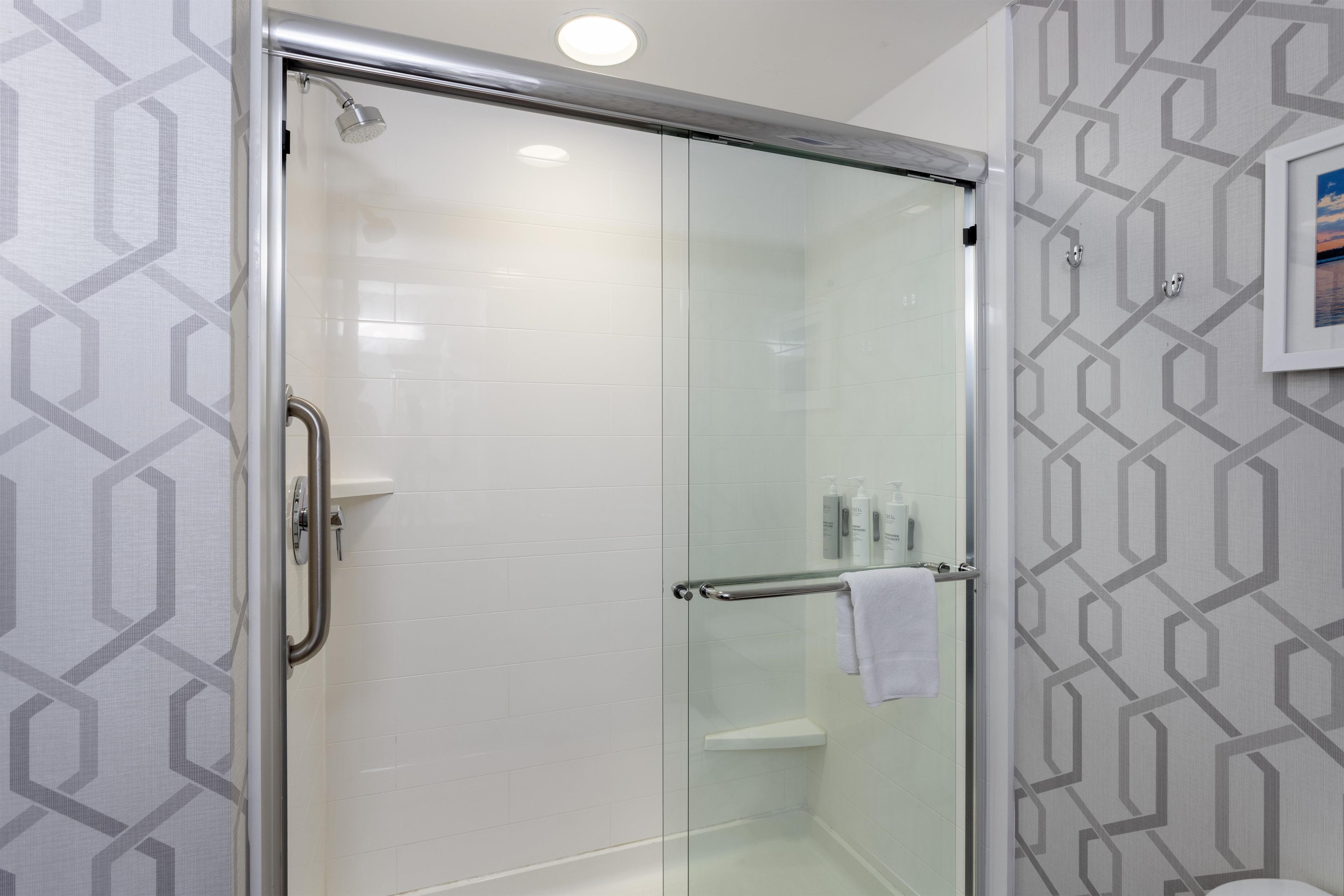 A glass-enclosed shower with a handrail, a white towel hanging on the door, and a geometric-patterned wall.