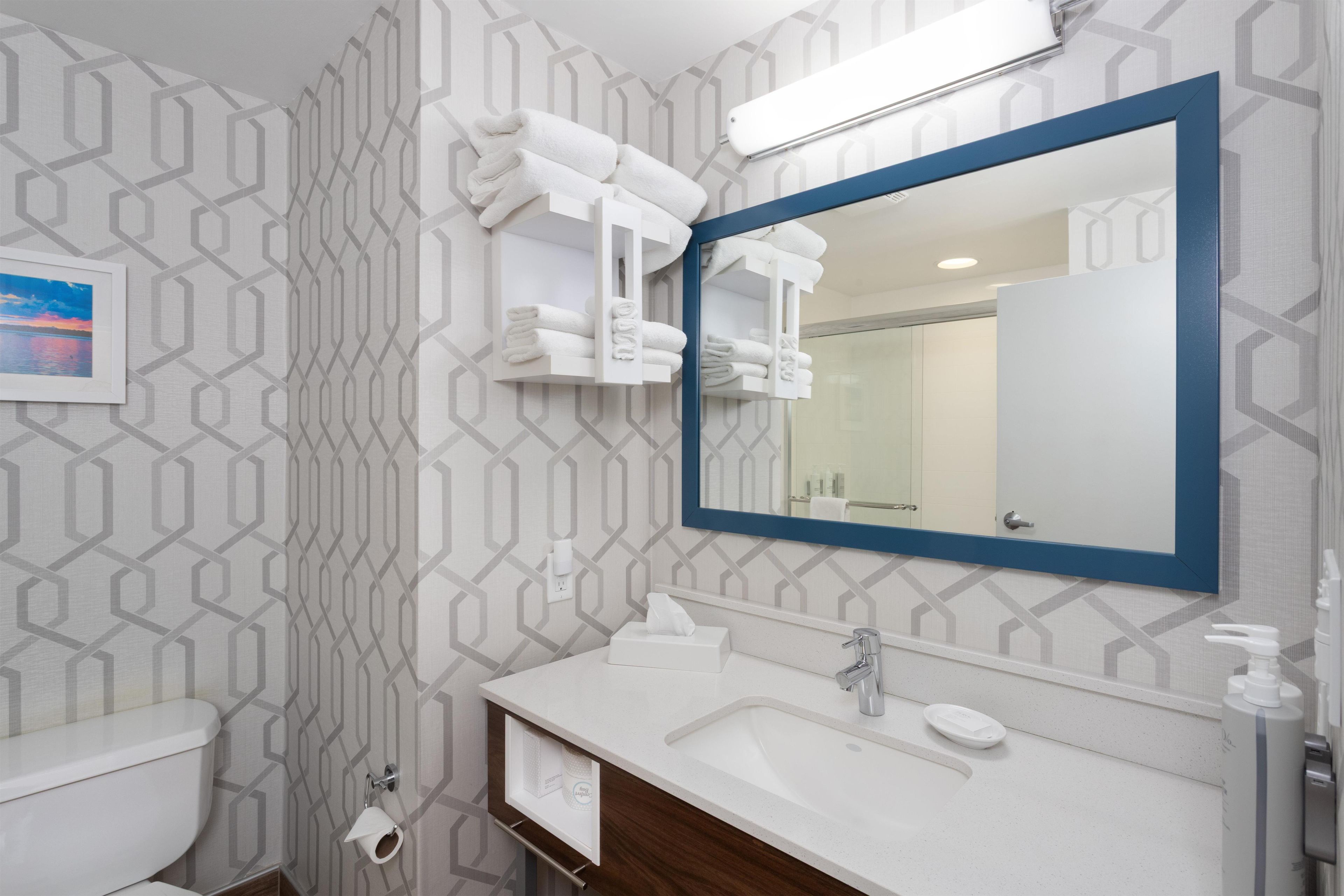 A bathroom with a white sink, a mirror with a blue frame, and a towel rack with folded towels.
