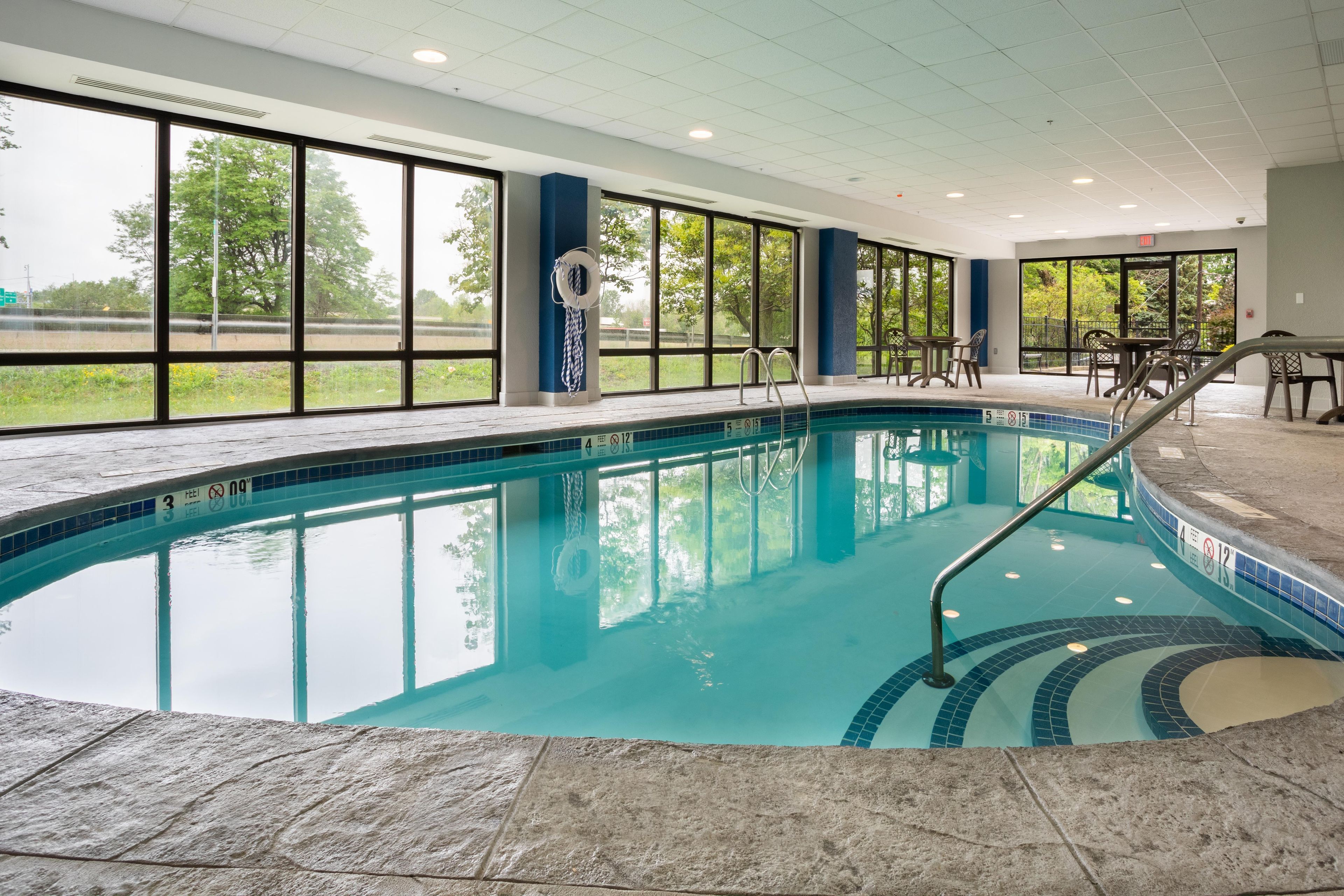An indoor swimming pool with clear water, a lifebuoy, and a pool ladder.