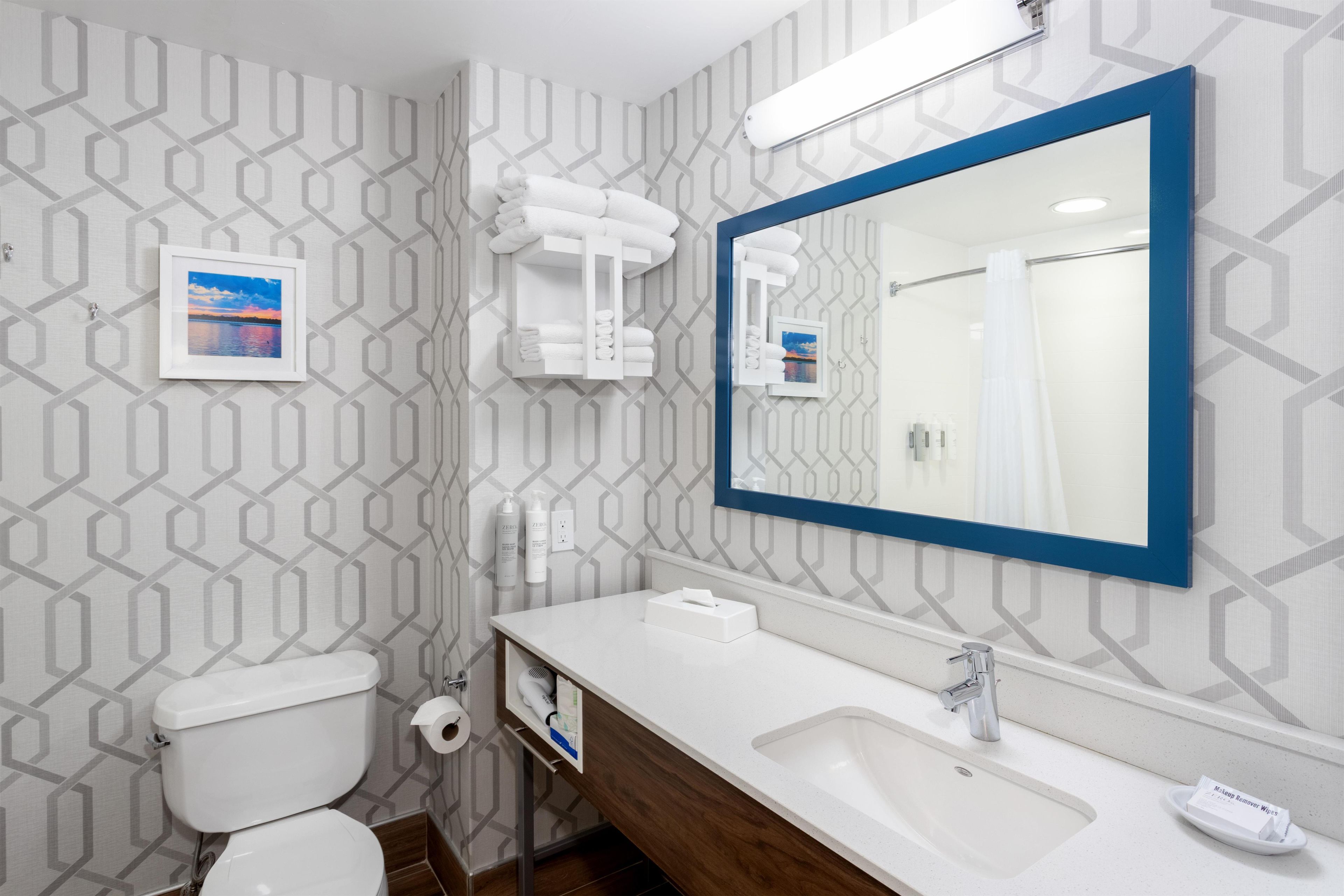 Un baño con inodoro, lavamanos, espejo, toallero y un cuadro en la pared.