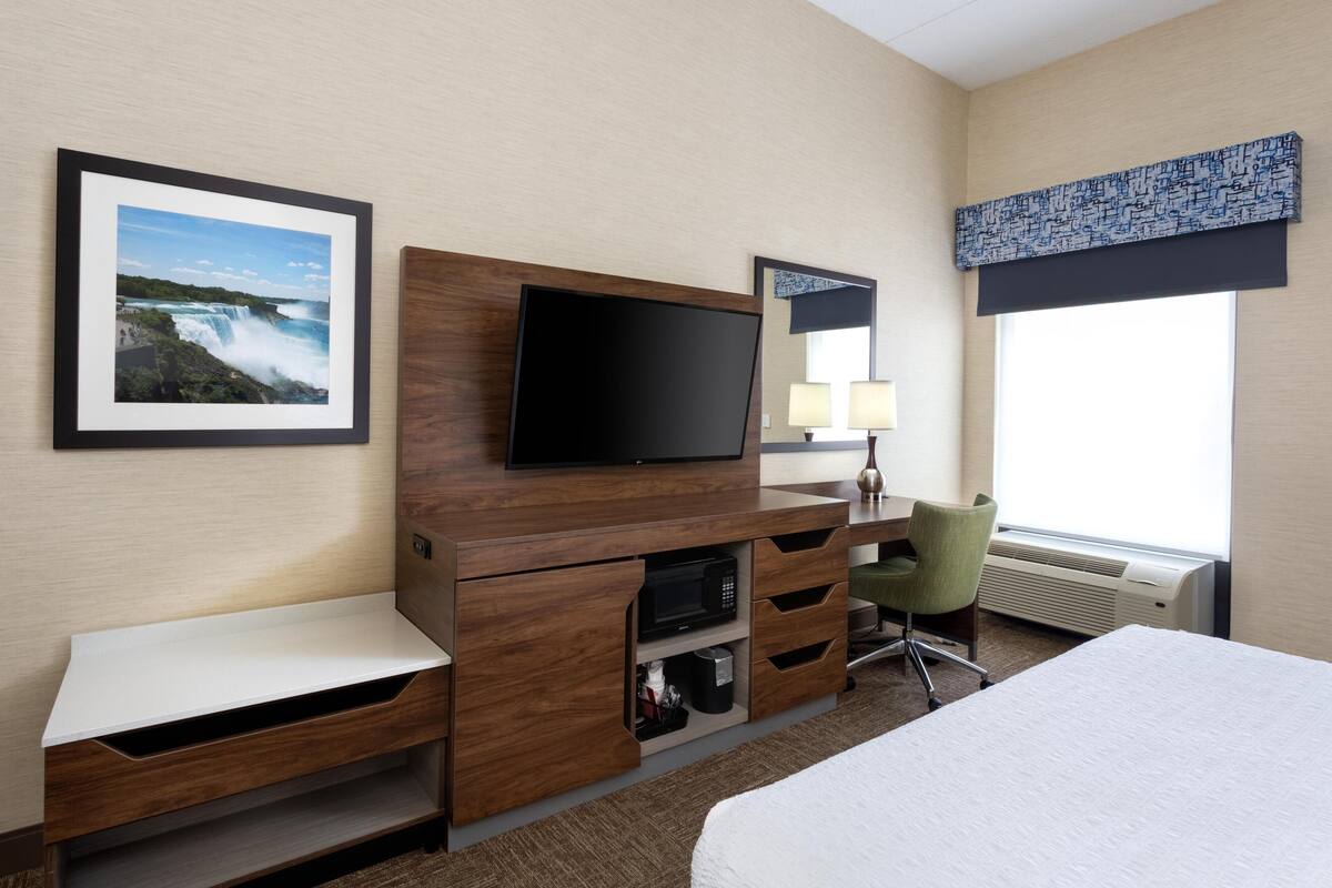 Une chambre d’hôtel comprenant un lit, un bureau avec un téléviseur à écran plat, une chaise, une fenêtre donnant sur un paysage agréable et un tableau encadré au mur.