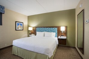 Una camera d'albergo con un letto, lampade sui comodini, un comodino, uno specchio e un quadro appeso al muro.
