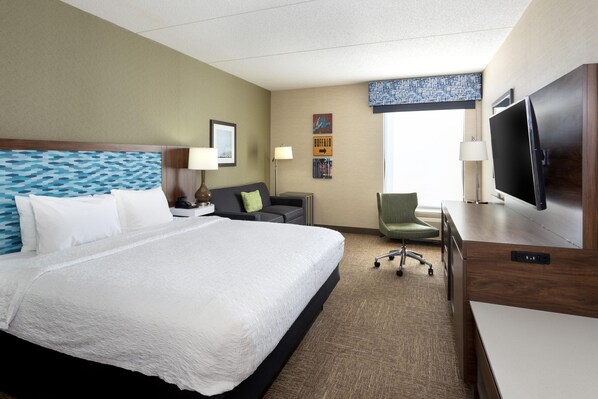 A hotel room with a large bed, a desk with a flat-screen TV, a chair, and a window with a view.