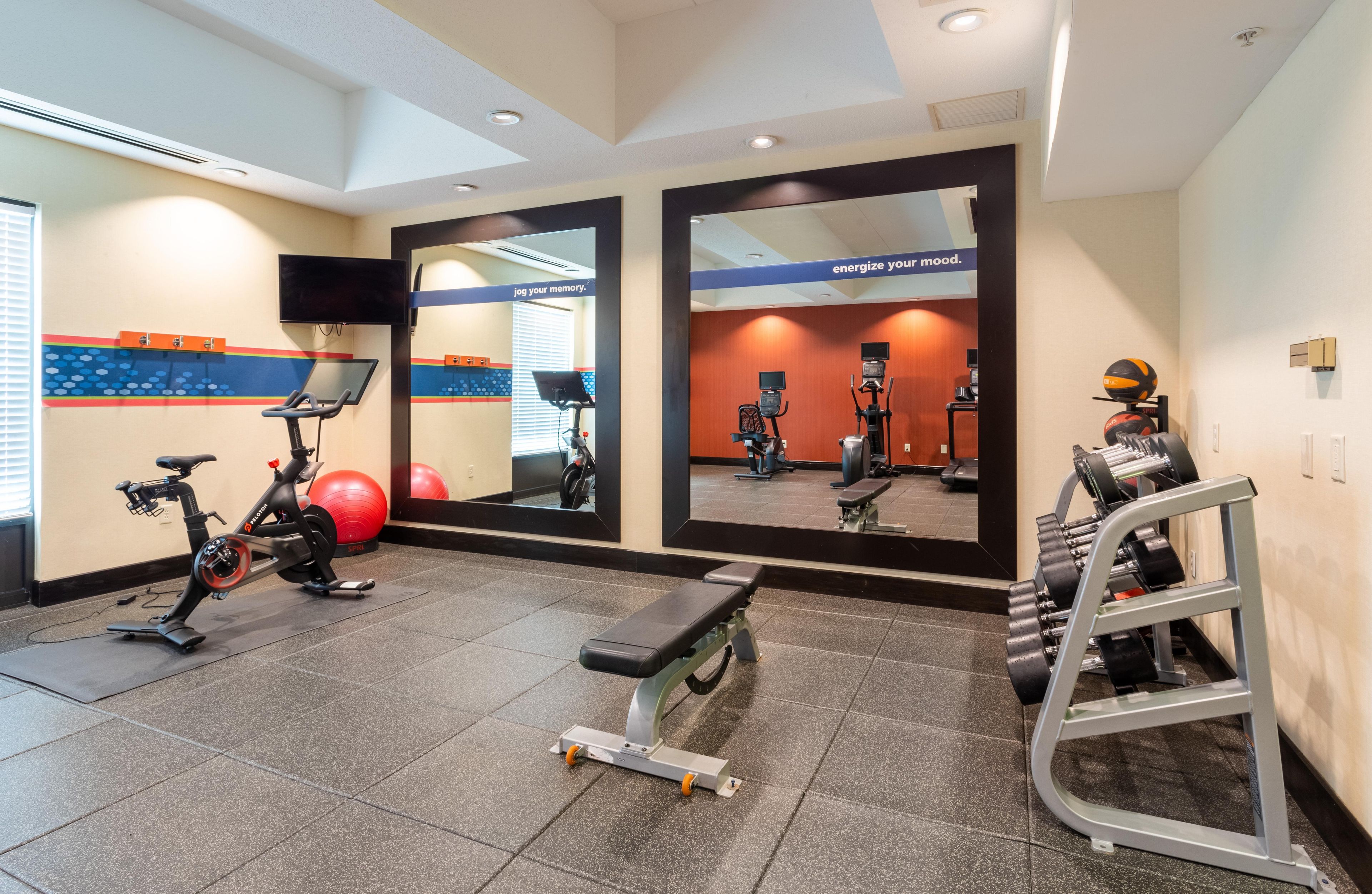 Academia com equipamentos de ginástica, um banco e um espelho.