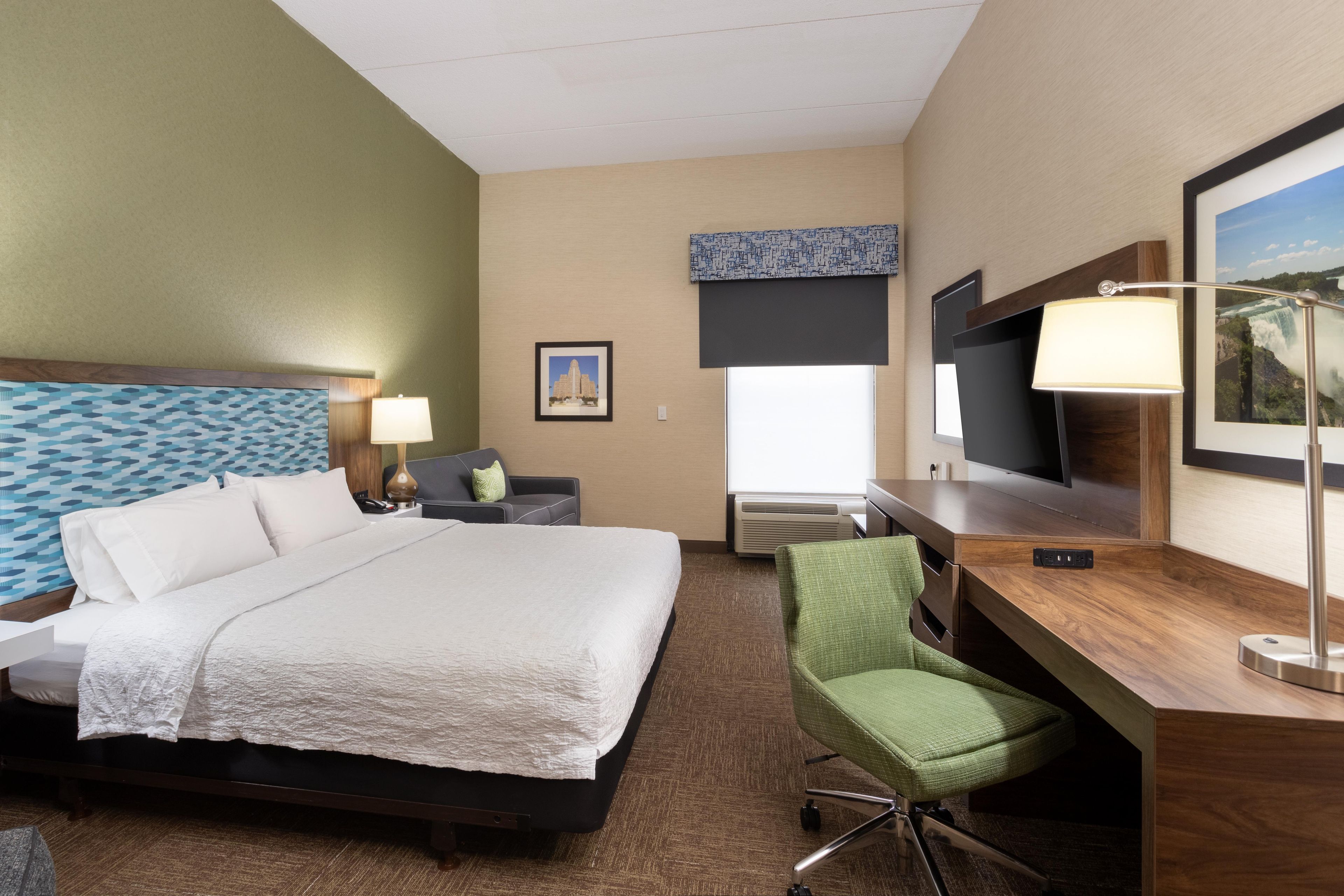 A hotel room with a bed, a desk, a chair, a TV, and a window with a view of a waterfall.