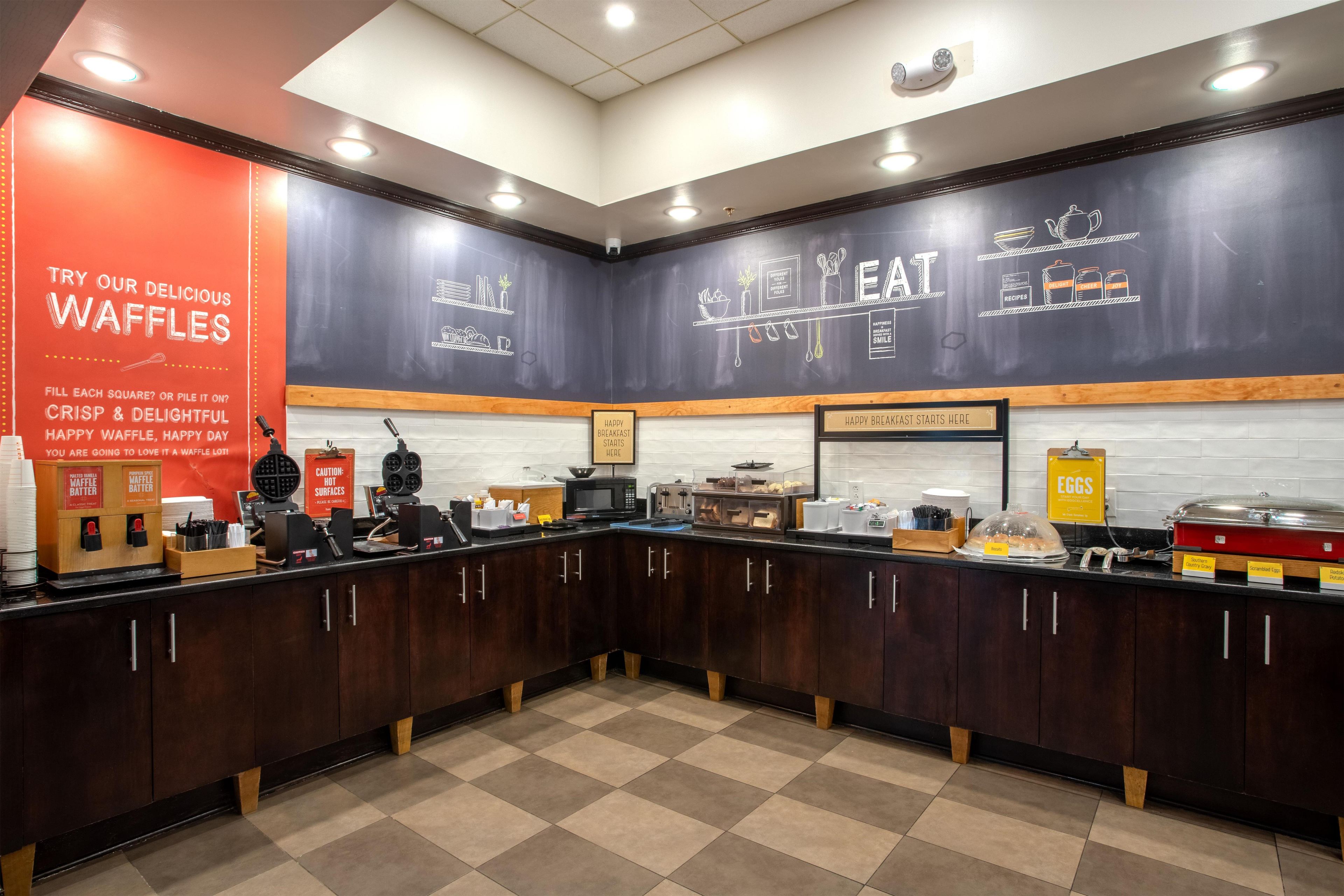 A breakfast area with waffle stations, a chalkboard menu, and various breakfast items displayed.