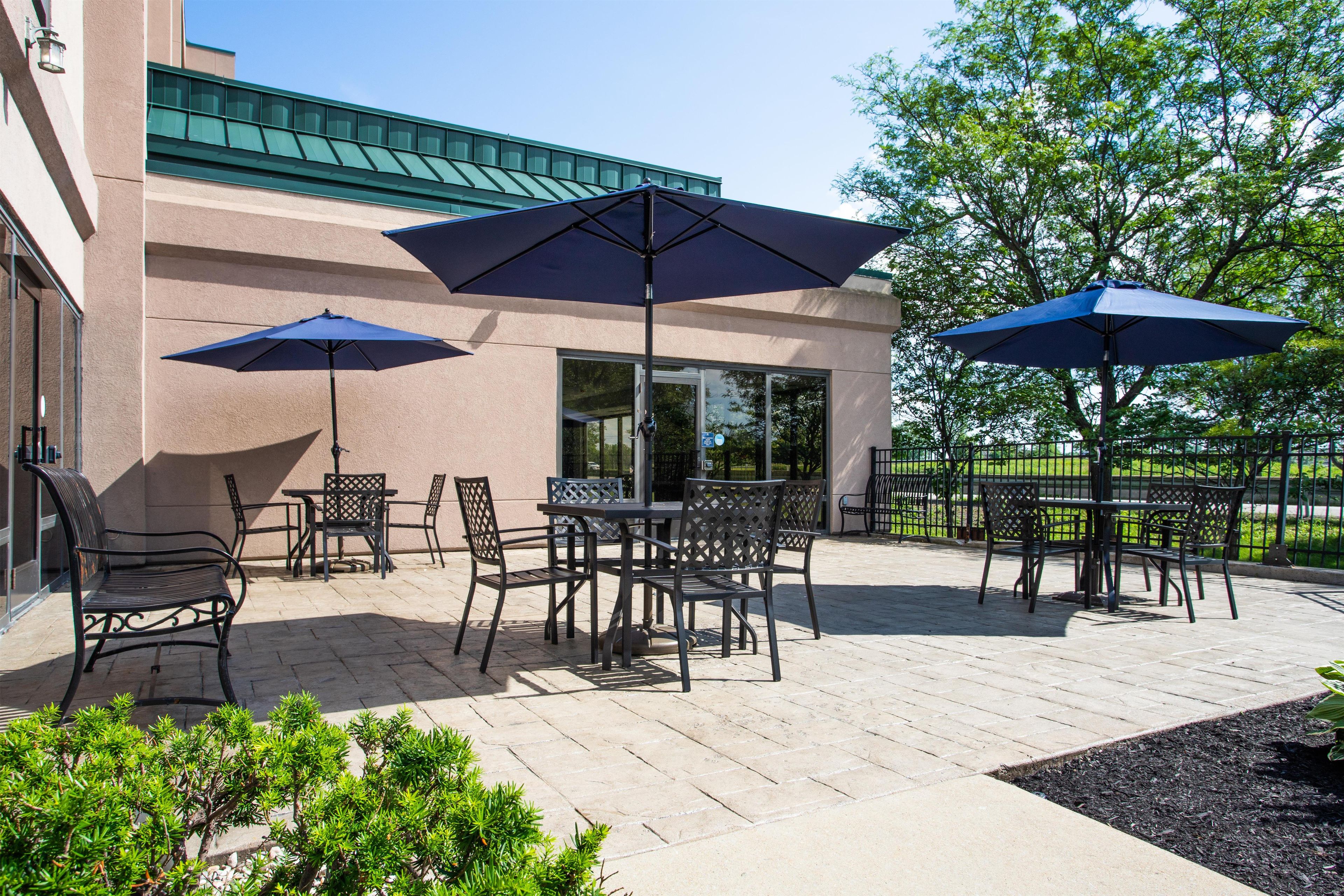 An outdoor patio area with tables and chairs, two umbrellas, and a building with a green roof.