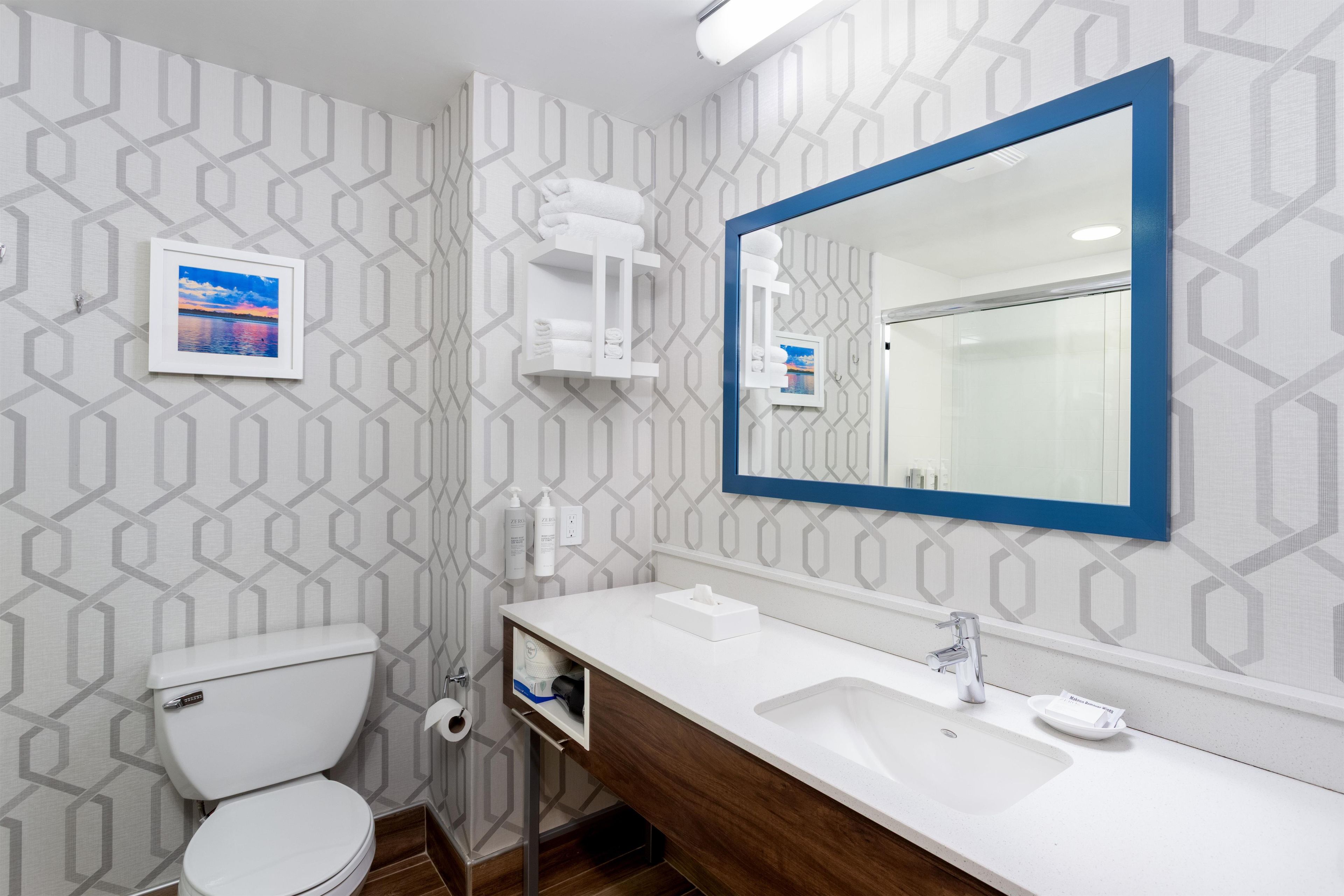 A bathroom with a toilet, sink, mirror, and towel rack.