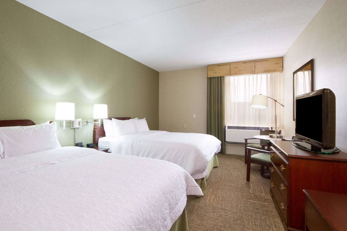 Une chambre d’hôtel avec deux lits, un bureau avec une télévision, une lampe et une fenêtre avec des rideaux.