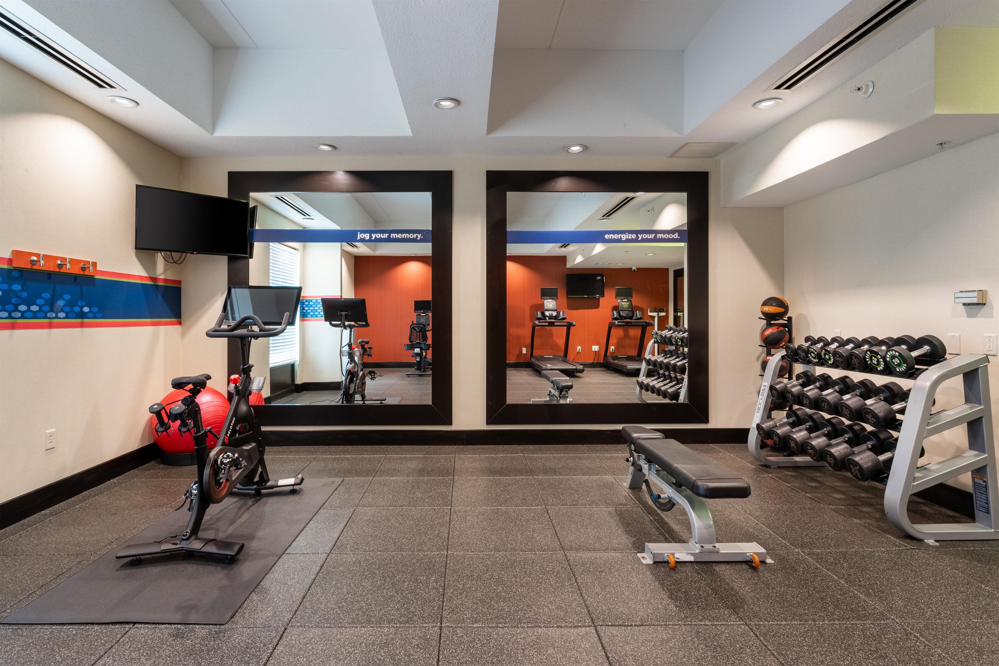 Een sportschool met trainingsapparatuur, spiegels en een televisie.