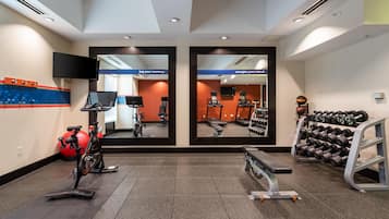 Een sportschool met trainingsapparatuur, spiegels en een televisie.