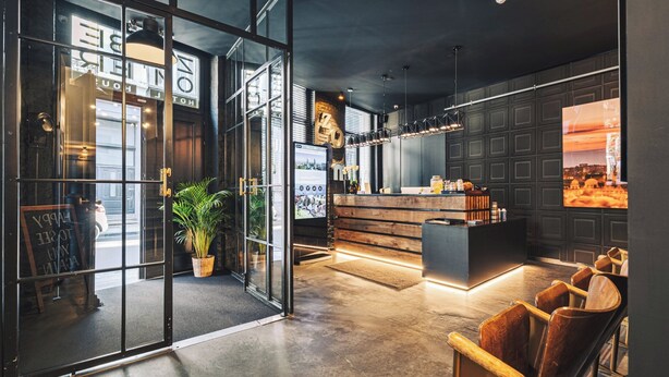 A modern interior with a reception desk, seating area, and a large window displaying a cityscape. - Zoom Hotel (Brussels)