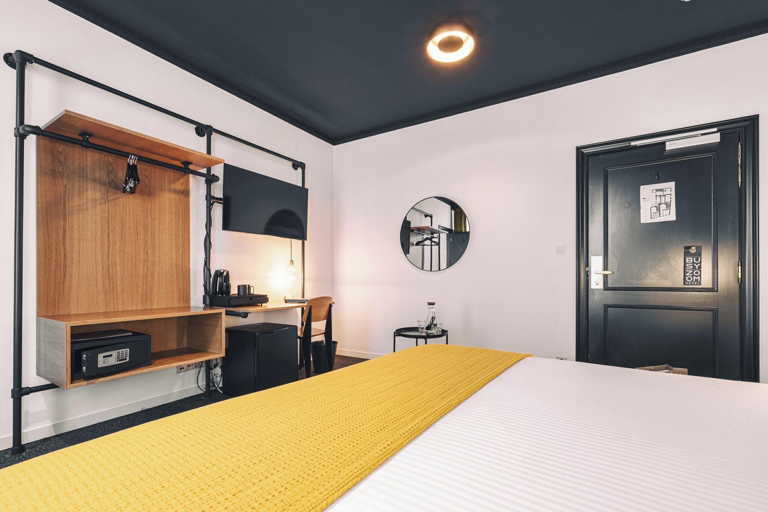 Ein Hotelzimmer mit Bett, Schreibtisch, Stuhl, einem kleinen Tisch, einem Spiegel und einer Tür mit Kartenleser.