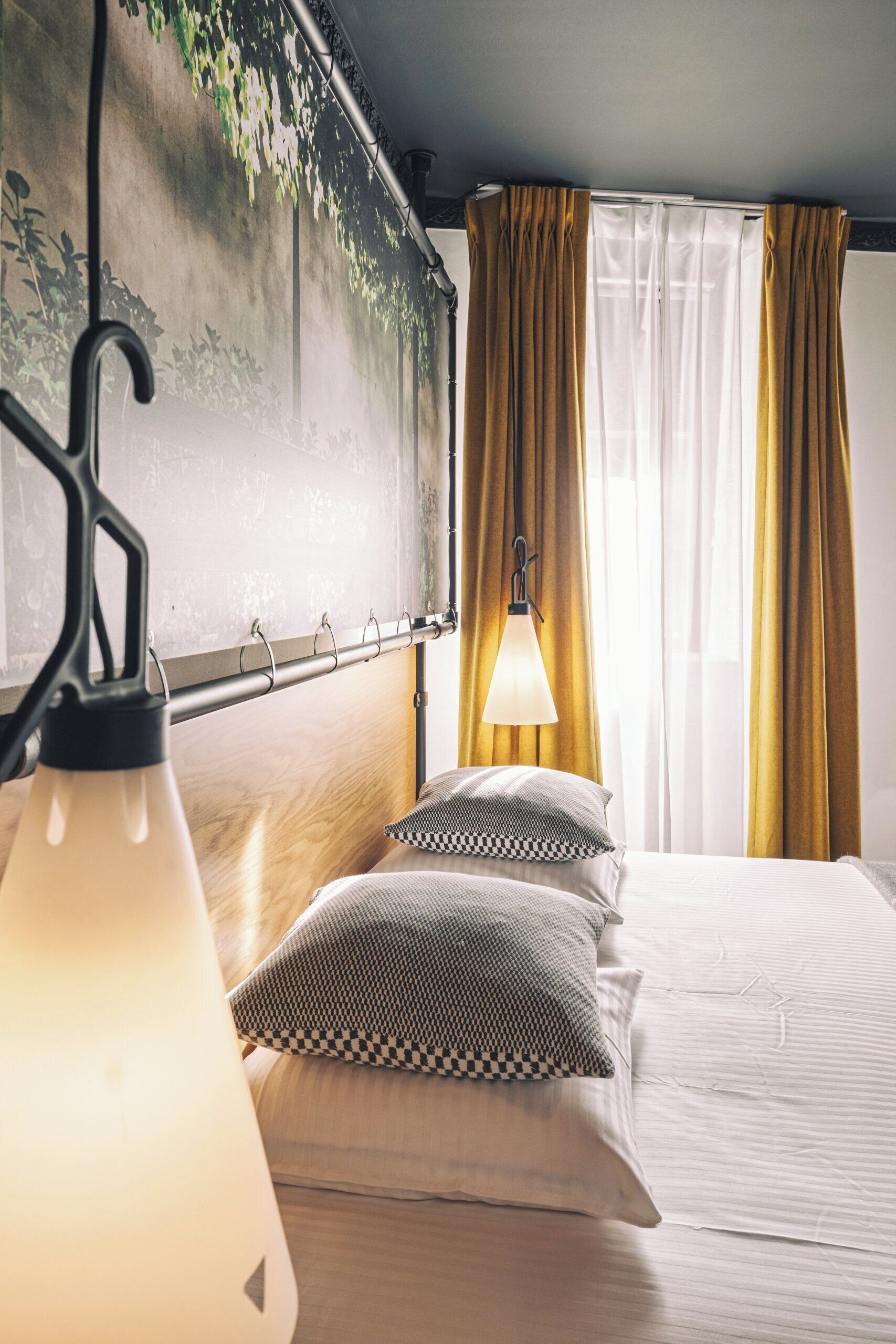 Een hotelkamer met een bed, een hanglamp, een wandlamp en een raam met gordijnen.