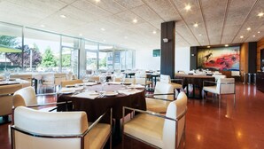 A spacious dining area with multiple tables and chairs, large windows, and a modern ceiling design. - Hotel Granollers (Granollers)