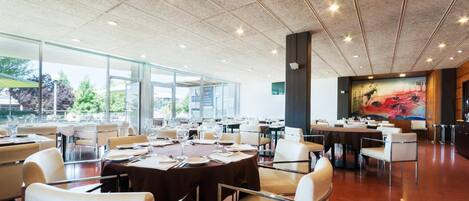 A spacious dining area with multiple tables and chairs, large windows, and a modern ceiling design.