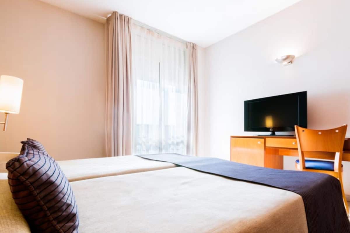 Habitació d'hotel amb dos llits, televisió, escriptori i una cadira.