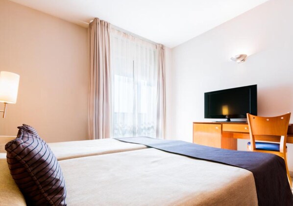 Una habitación de hotel con dos camas, televisión, escritorio y una silla.