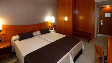 A hotel room with a double bed, wooden headboard, bedside tables, a bench, and a wardrobe.