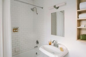 A modern bathroom with white subway tiles, a glass shower enclosure, a white sink with a mirror above it, and a wooden shelf with towels. - Hotel Beverly Terrace - Beverly Hills/West Hollywood (Beverly Hills)