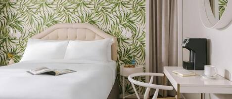 A hotel room with a bed, a small table with a chair, a coffee machine, and a mirror on the wall.