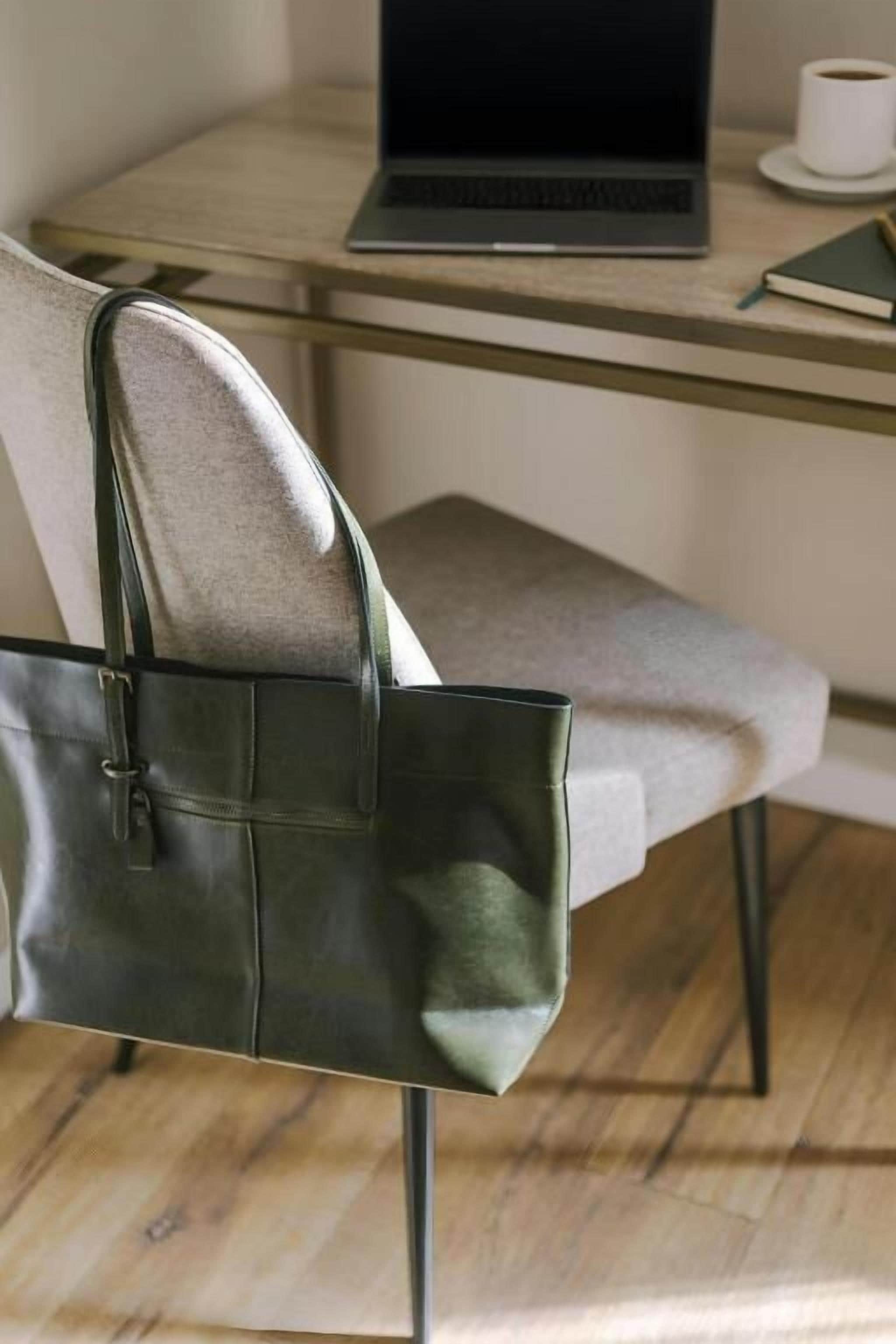 A chair with a dark green handbag on it, a laptop on a table, and a cup of coffee.