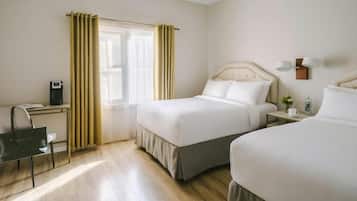 A hotel room with two beds, a desk with a chair, a bedside table with a lamp, and a window with curtains.