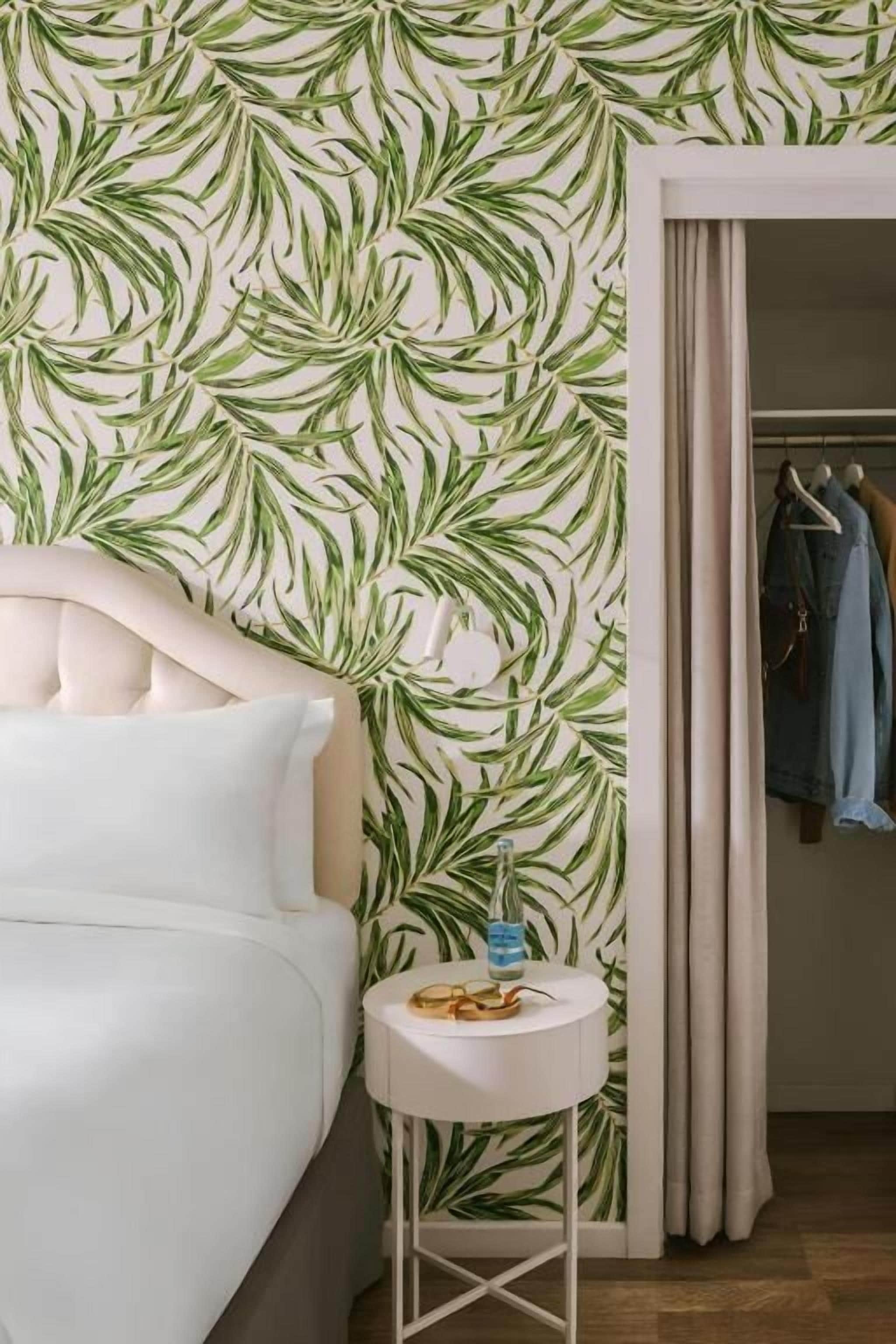 Une chambre à coucher comprenant un lit, une petite table ronde, une armoire et un mur orné d’un motif végétal.