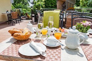 Une table dressée pour le petit-déjeuner, avec du pain, du jus et une carafe, installée à l’extérieur.